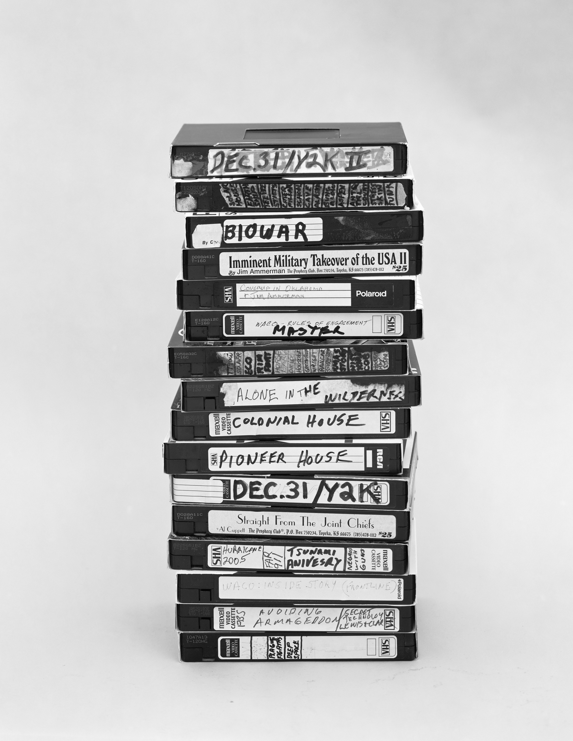 Black and white photograph of a stack of VHS tapes each labeled in handwriting