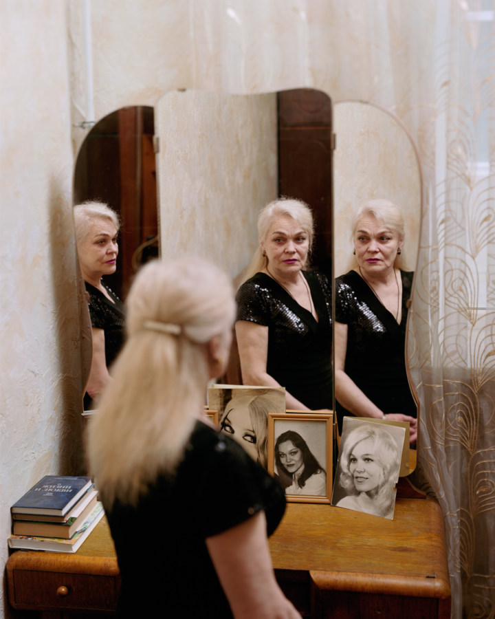 A photograph of an elderly woman looking at herself in the mirror, with three reflections.