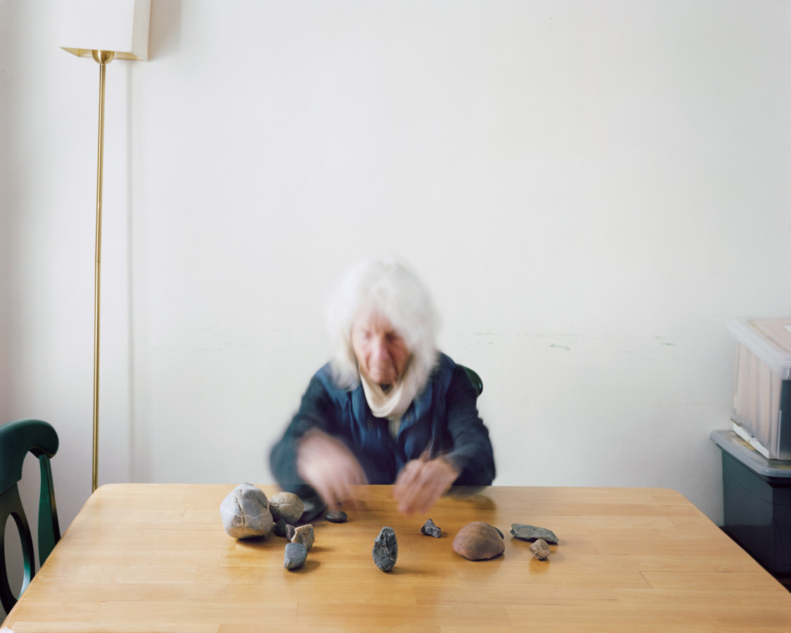 A photograph of a woman, blurred by movement, arranging stones in a circle on a table