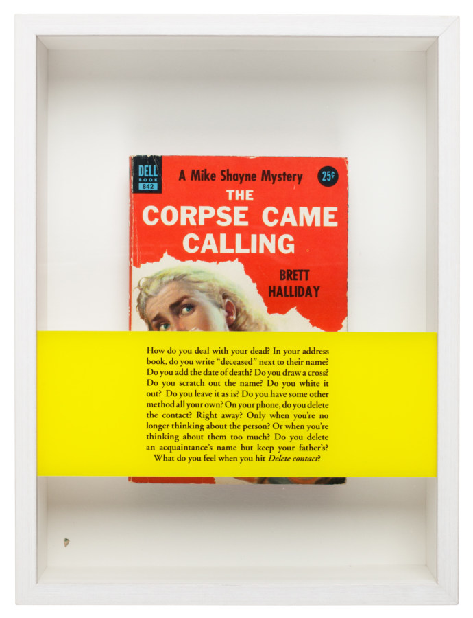 A red paperback book, framed in a white box with a yellow banner of text across the glass of the frame.