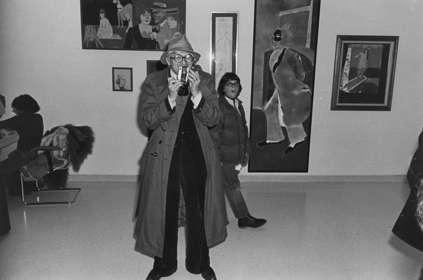 Black and white photograph of a man holding a camera in an art gallery