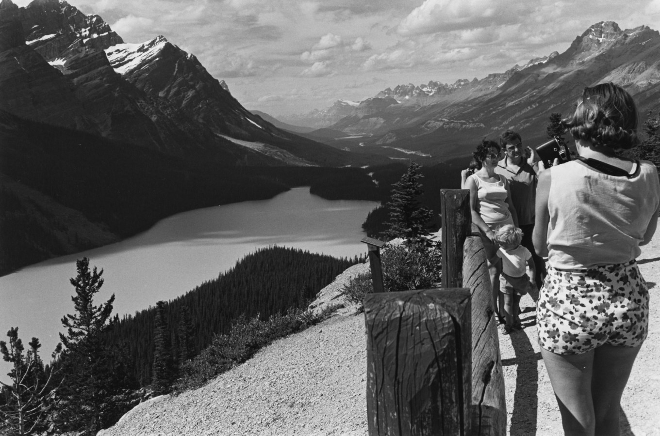 Black and white photograph of tourists having their photograph taken in front of a valley