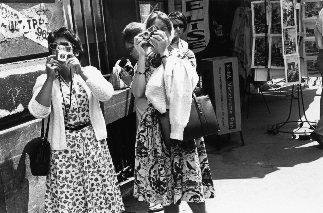 Black and white photograph of two women taking photographs on a city sidewalk