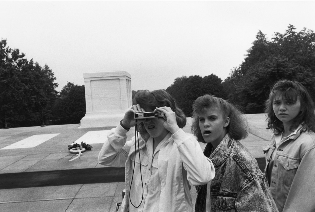 Black and white photograph of three young women in front of a stone memorial taking a photograph