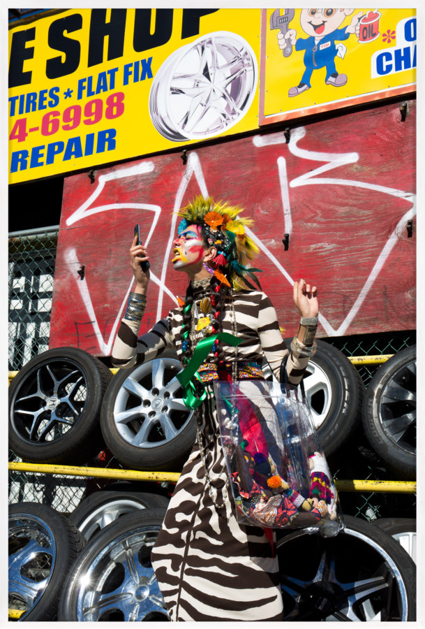 Framed color photograph of an eclectically dressed person posing in front of a tire shop