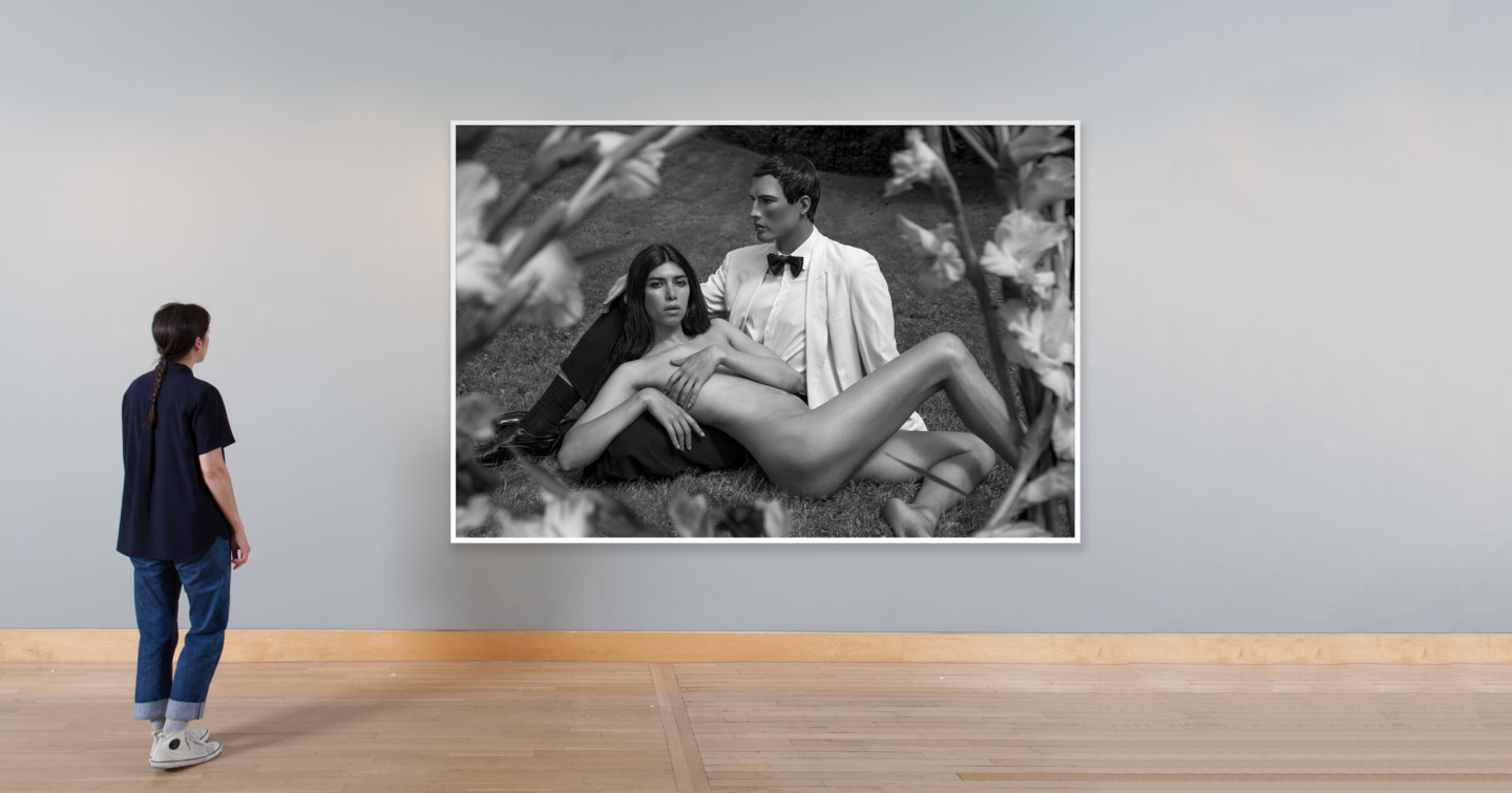 Installation photograph of a black and white photograph of a reclining nude woman leaning against a male mannequin in a suit