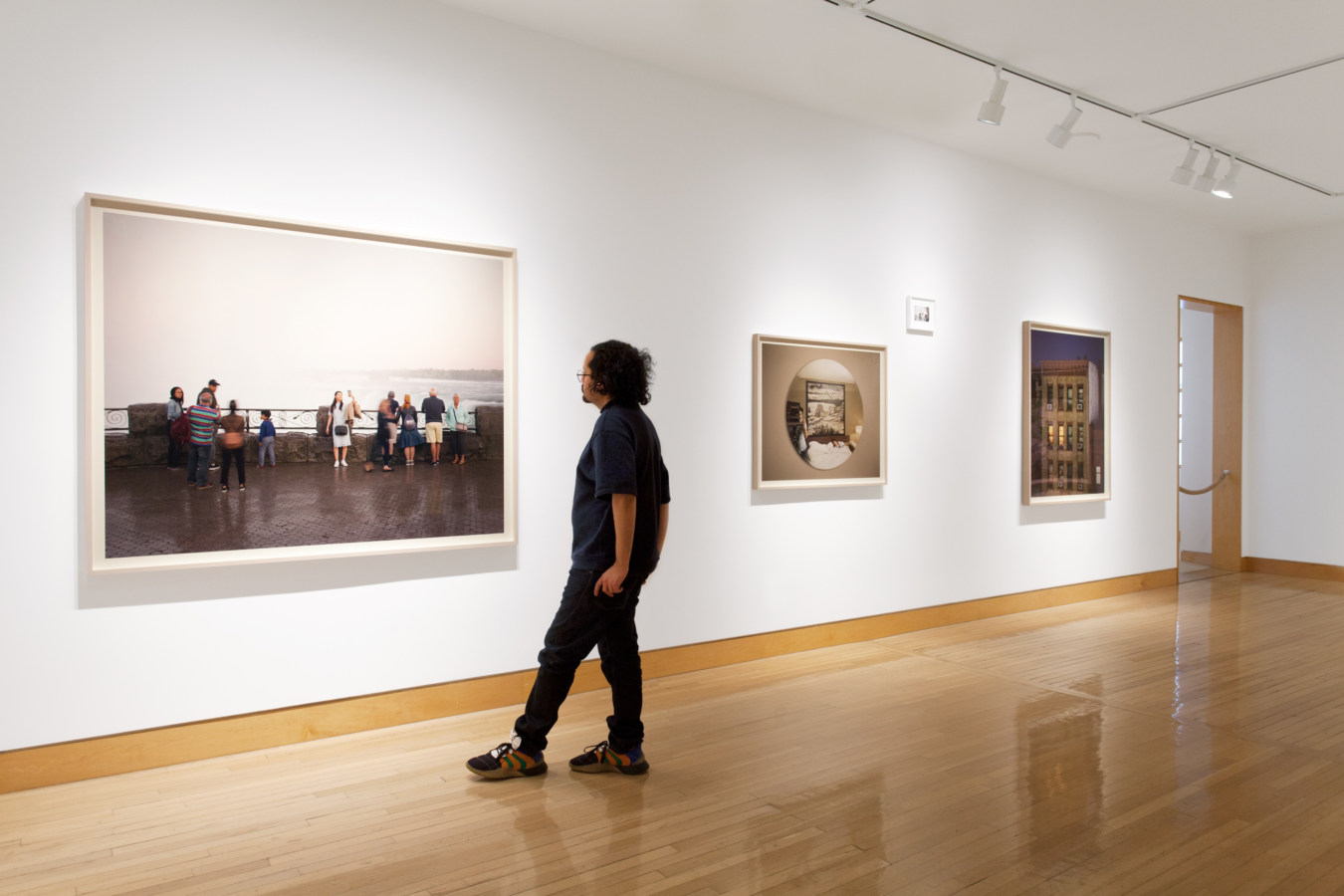 Color image of color photographs on white gallery wall with person viewing artwork