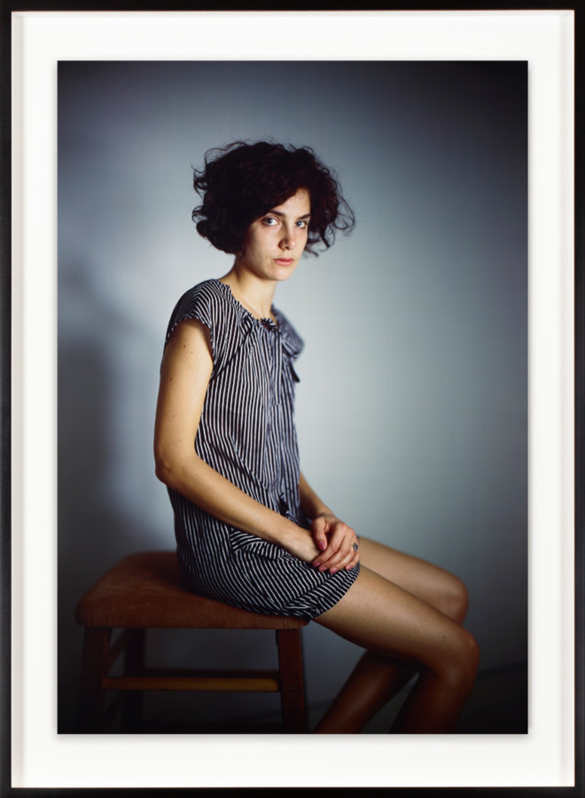 Framed color photograph of a woman in a striped dress seated on a stool