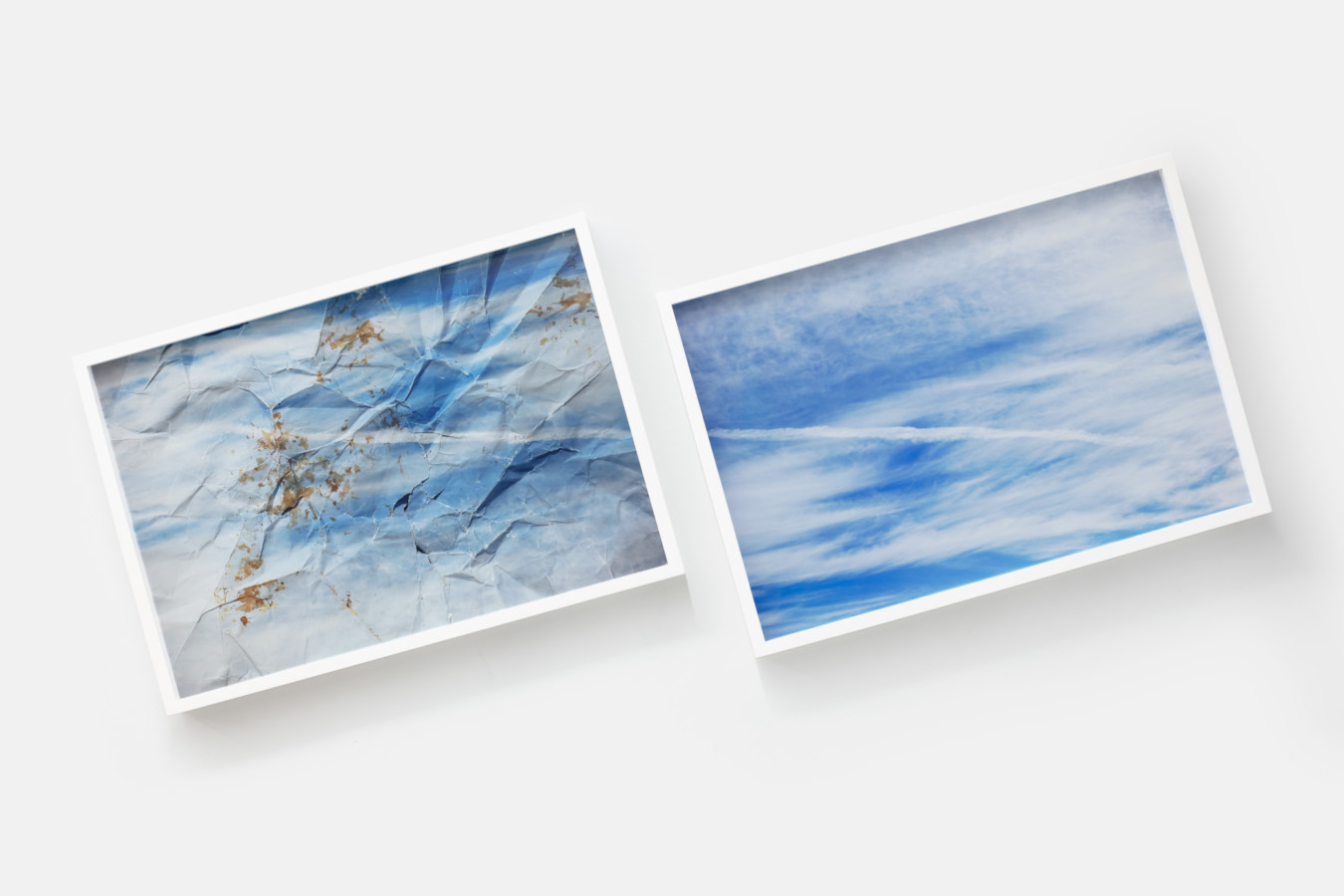 Two framed color photographs of a blue sky with wispy clouds hung at a tilted angle
