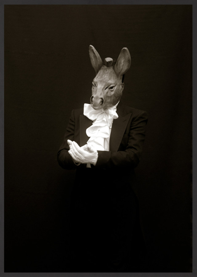 Framed black and white photograph of suited figure with white gloves wearing a mask depicting a donkey