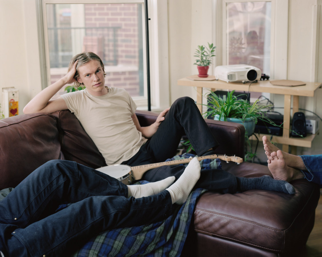 Color image of a reclined male on leather sofa with two pairs of legs also in frame