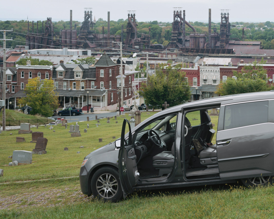 Color image of minivan in cemetery with furnace plant in background