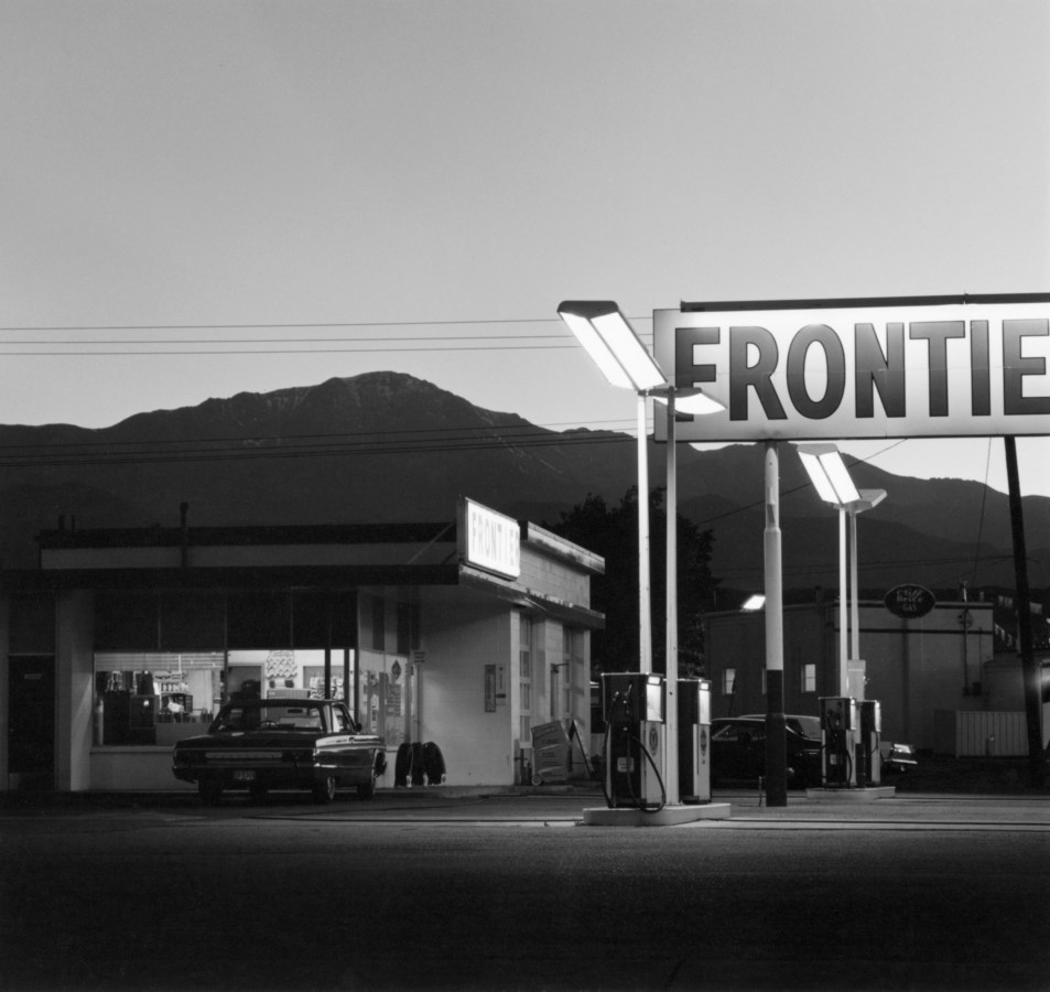 Black and white photograph of gas station exterior with mountainous background