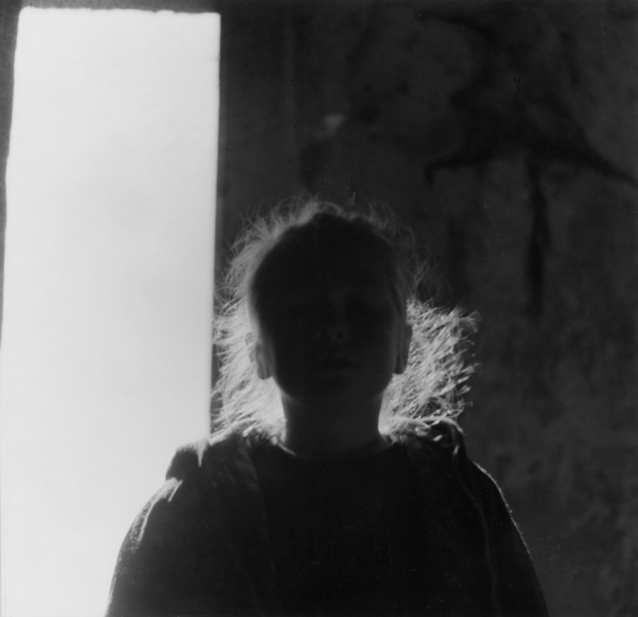 Black and white photograph of young girl backlit by exterior light