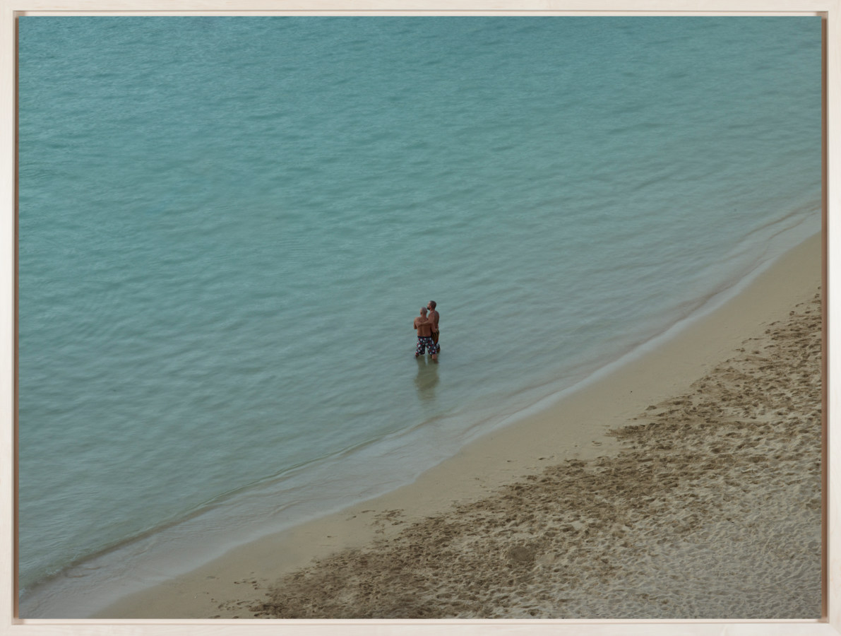 Color photograph of two men standing in knee-deep water near the shore of a calm sea
