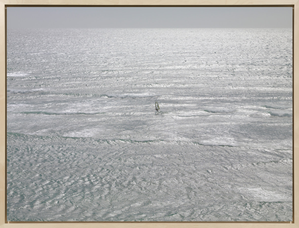 Color photograph of a lone windsurfer on a choppy silver sea