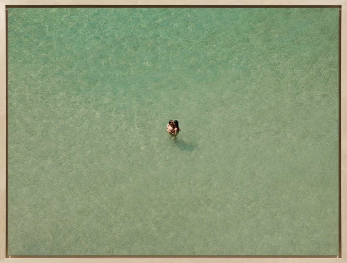 Color photograph of a couple embracing in an expanse of water.