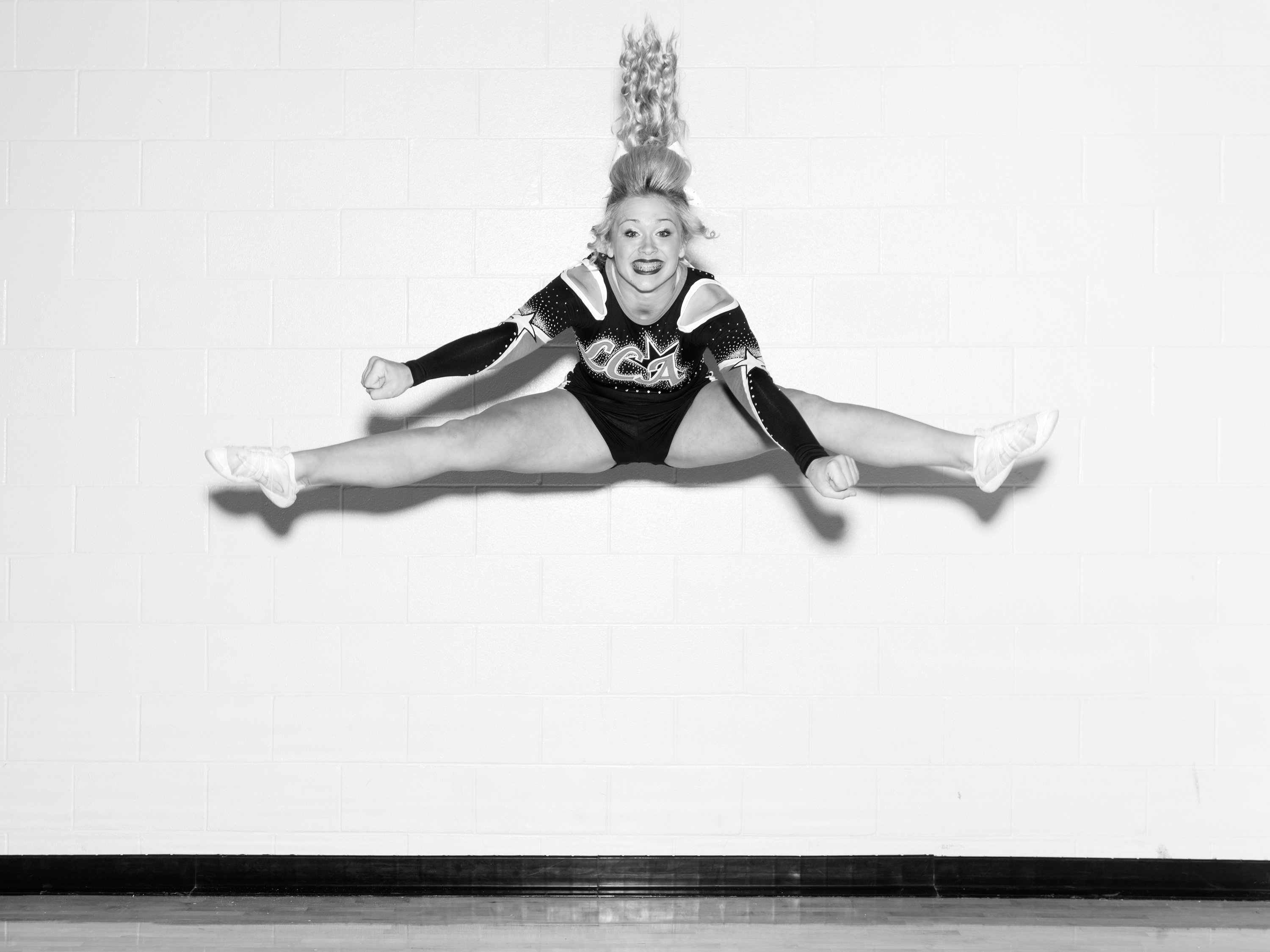 Black and white photograph of cheerleader in midair split