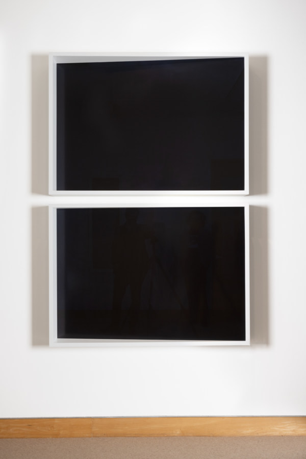 Color photograph of diptych of black photograms framed in white on white gallery wall