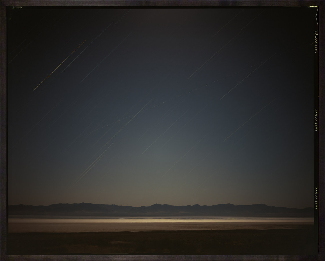 Color photograph of desert horizon at night with light trails from stars in dark walnut frame