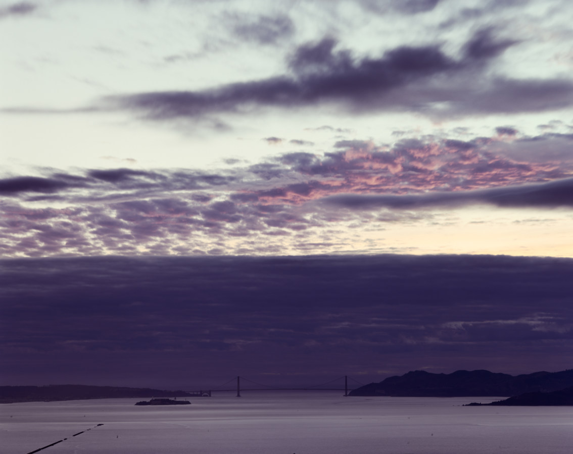 Color image of bay and Golden Gate Bridge under dark blue and pinkish clouds