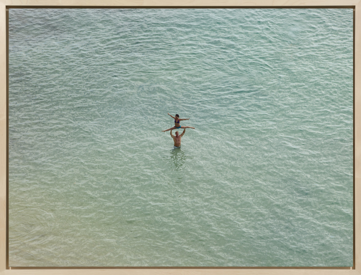Color photograph of two people in water doing acrobats taken from above in bleached wooden frame