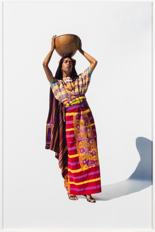 Framed color photograph of woman in culturally specific outfit holding a bowl atop her head