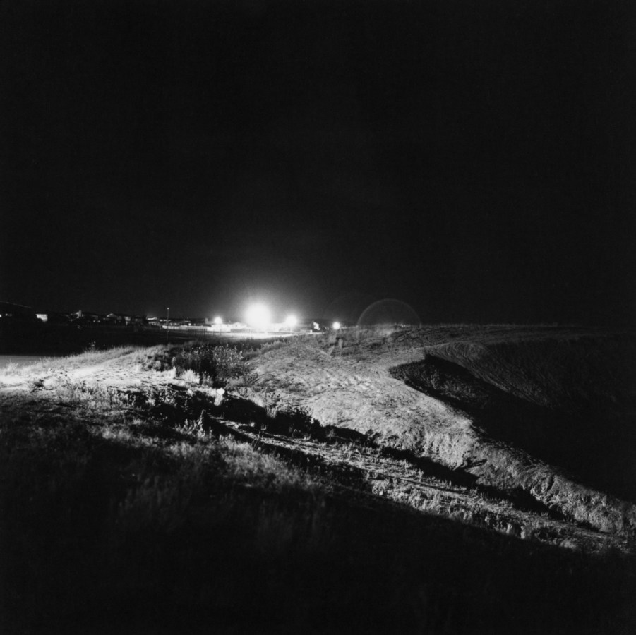 Black and white photograph of construction lights on at night in distance
