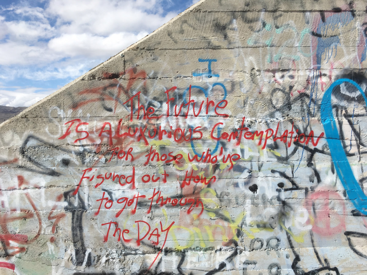 Color image of graffiti on brick wall with cloudy sky and mountains in partial view