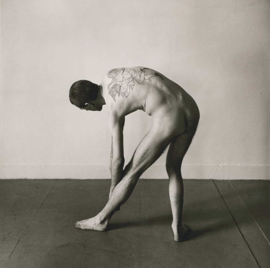 Black and white photograph of a man stretching while nude