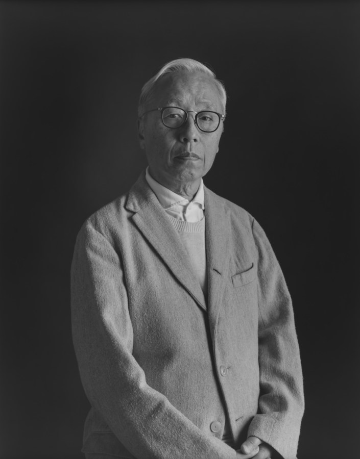 A black and white portrait of a person wearing a blazer and glasses