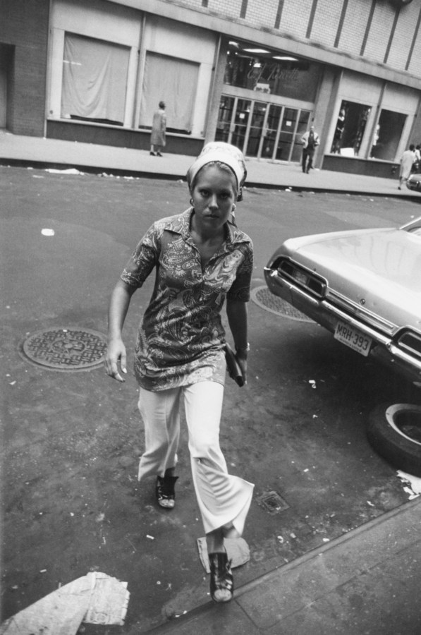 Black and white photograph of a woman in a paisley shirt stepping onto the curb from the street.