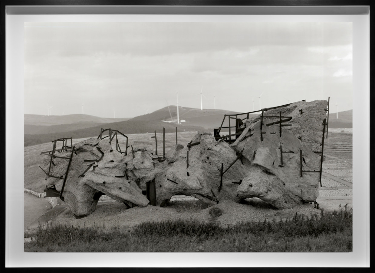 Black and white photograph of a large metal and concrete structure situated on hillside framed in black