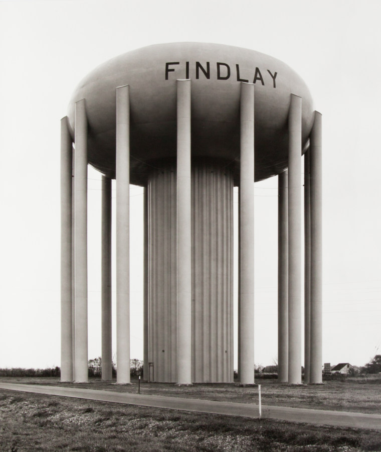 A black and white photograph of a large water tower with the word FINDLAY painted on the facade