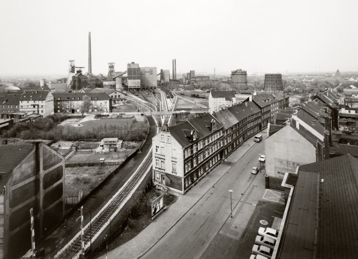Black and white photograph of a town strip with industrial plant on the horizon