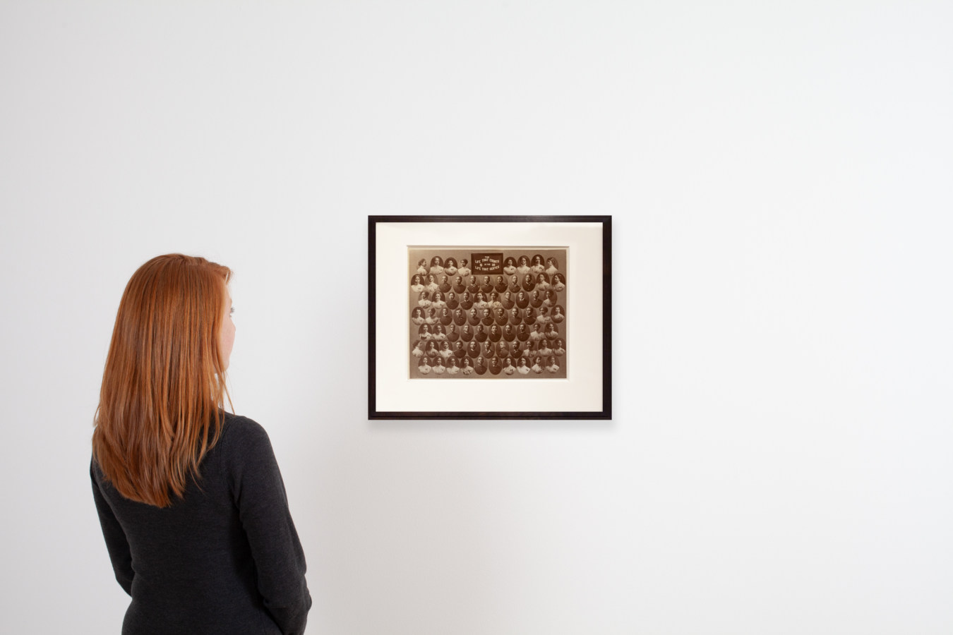 An image of a person looking at a framed photograph on a white wall
