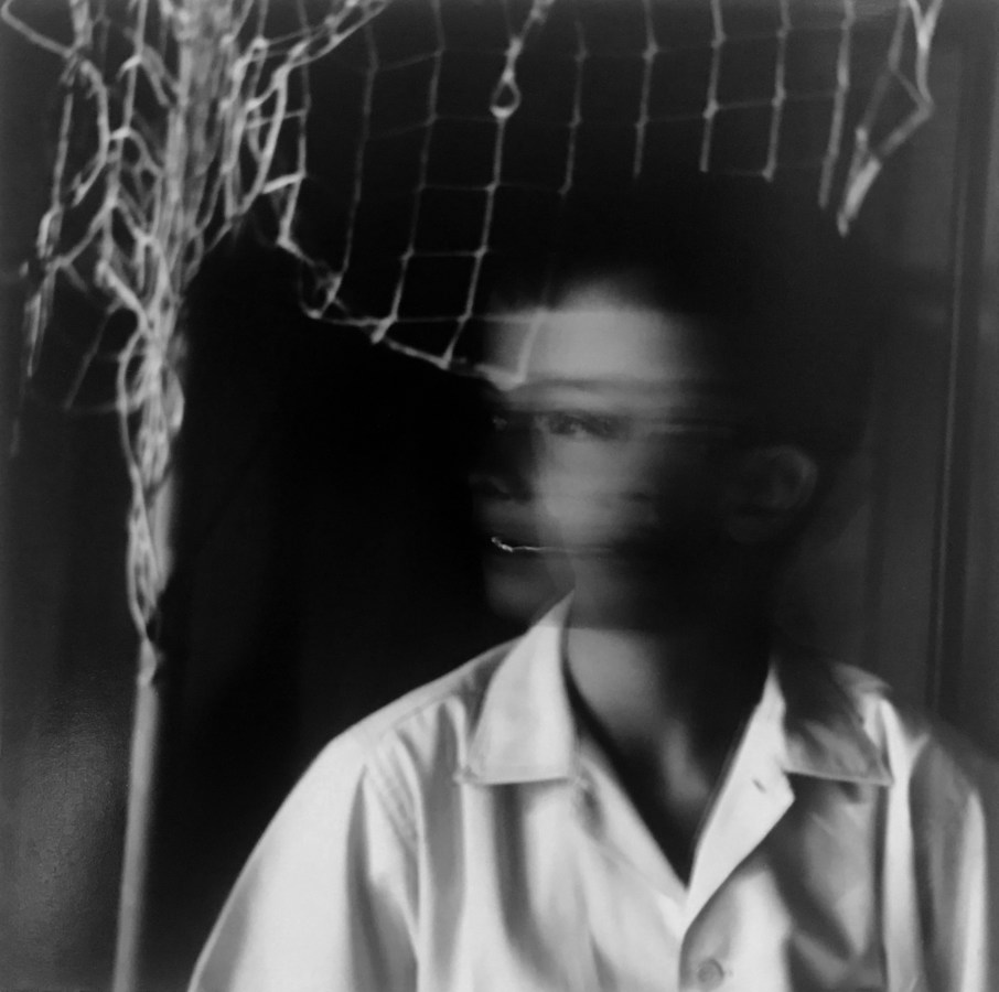Black and white photograph of a young boy in a white button up shirt, apparently caught mid-motion so that his face is shown in both blurred profile and straight on.