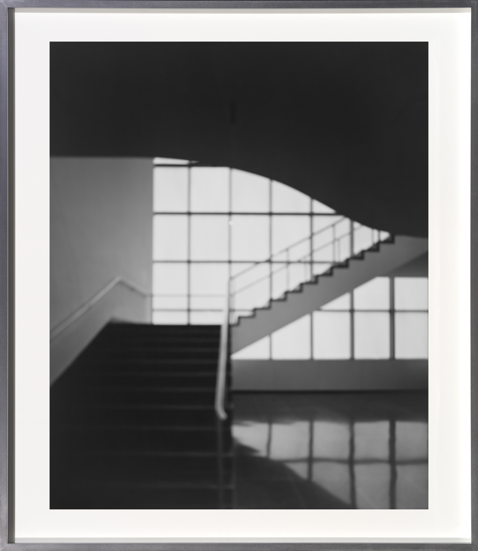 A framed black and white photograph depicting a blurry stairwell and window