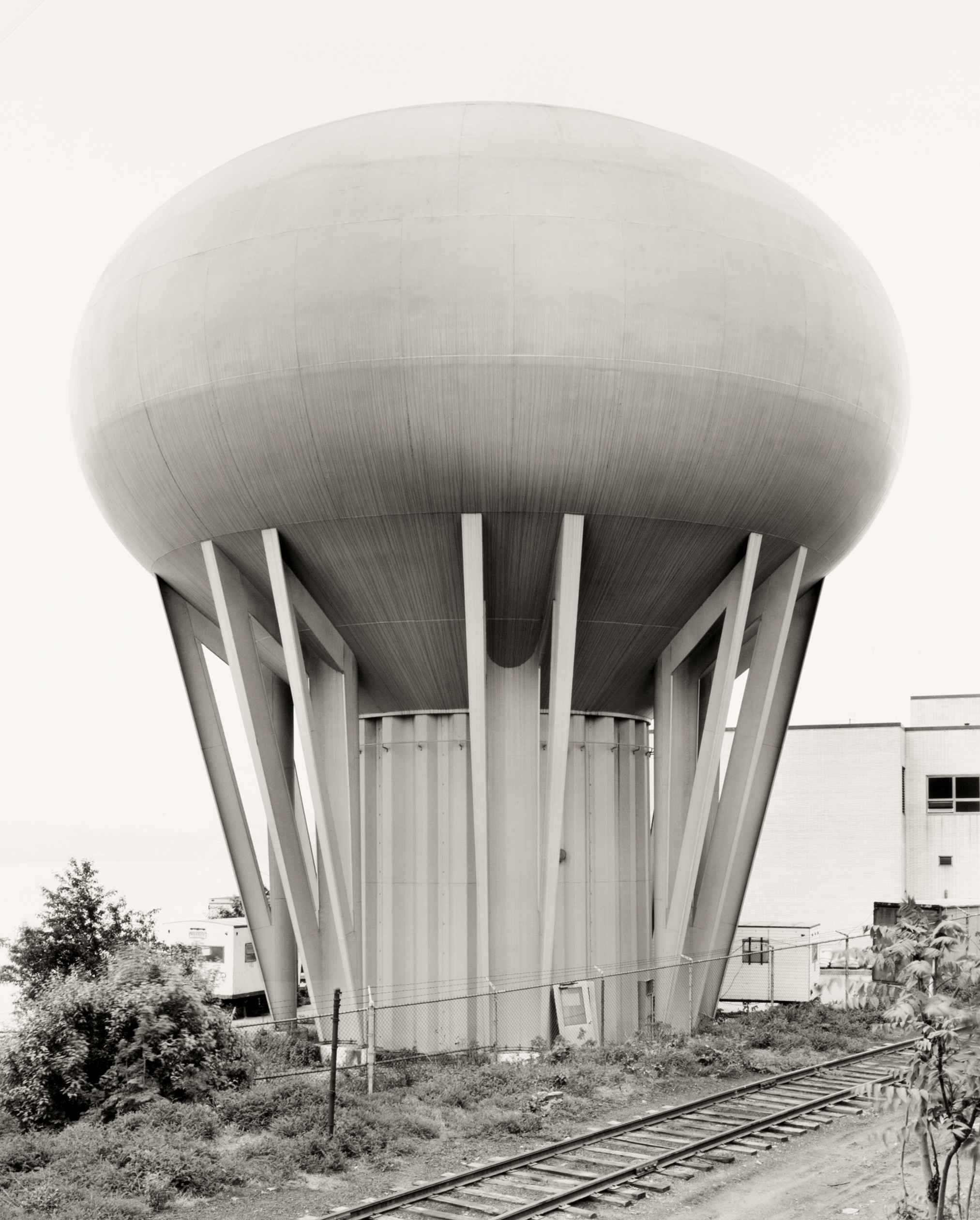 Black and white photograph of a circular water tower near railroad tracks