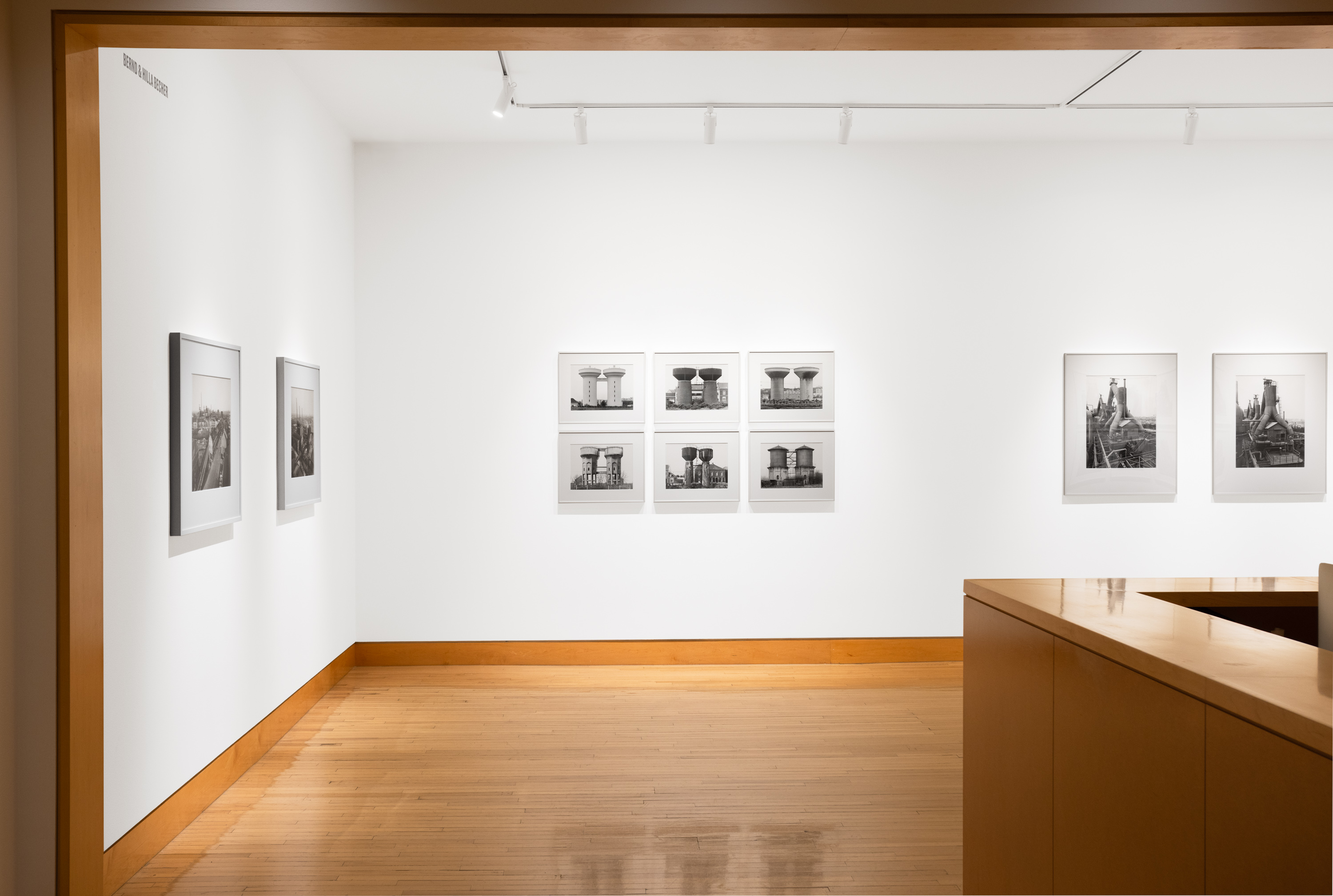 Color image of black and white photographs of water towers and landscapes, framed in white on white gallery walls