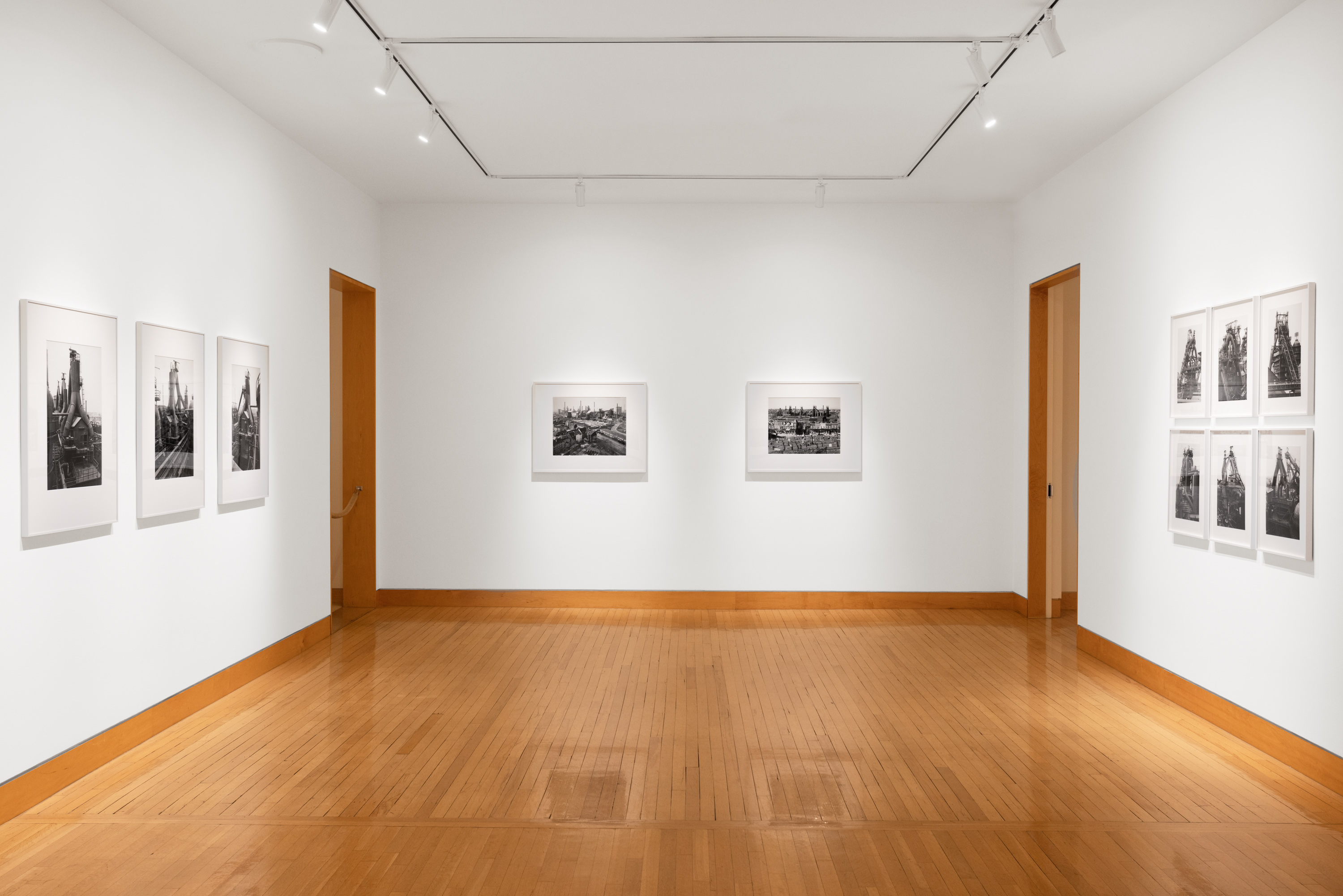 Color image of black and white photographs of industrial furnaces and landscapes, framed in white on white gallery walls