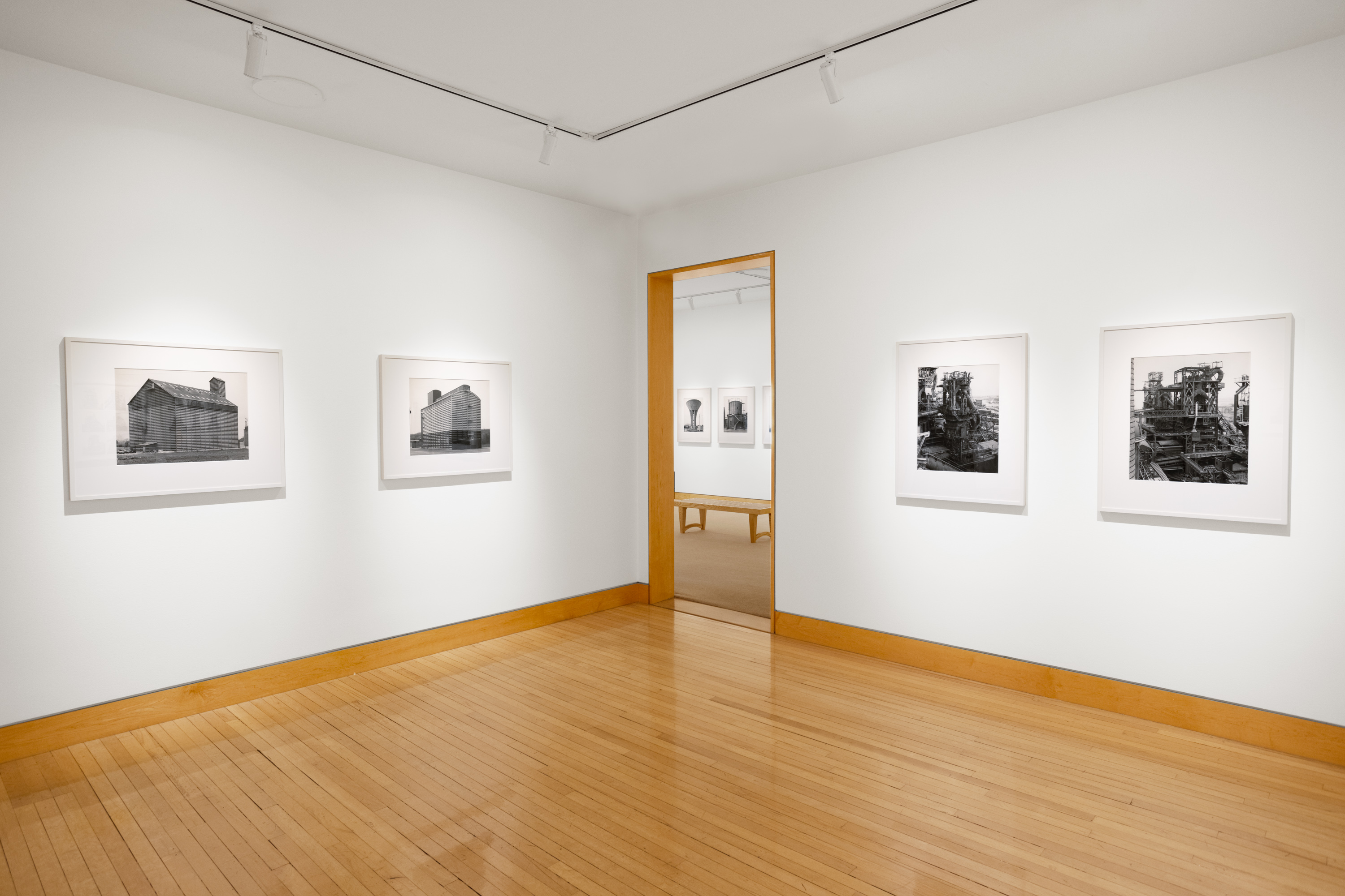 Color image of black and white photographs of various water towers and grain silos framed in white on white gallery walls