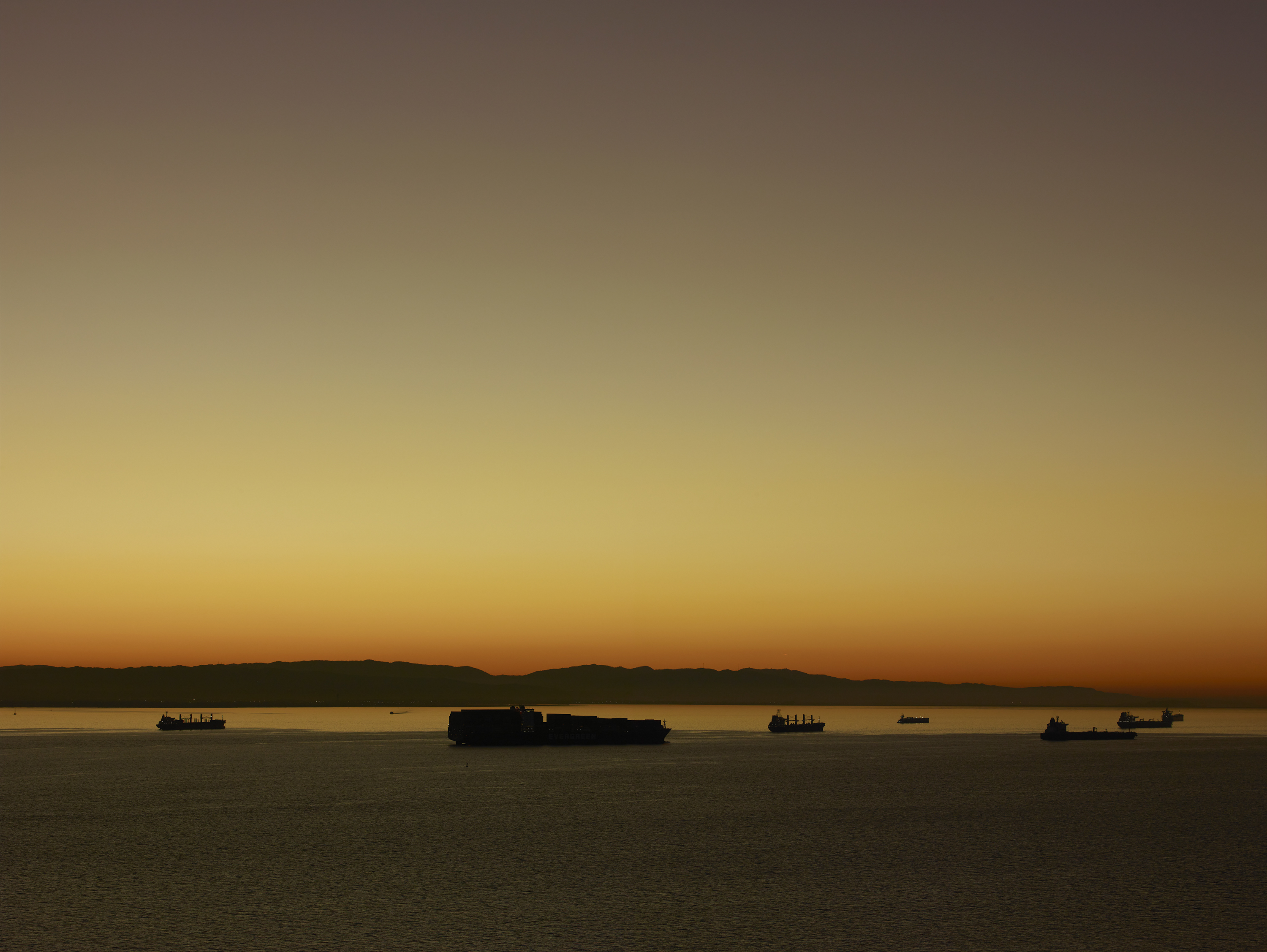 Color photograph of cargo ships on the water during a sunrise