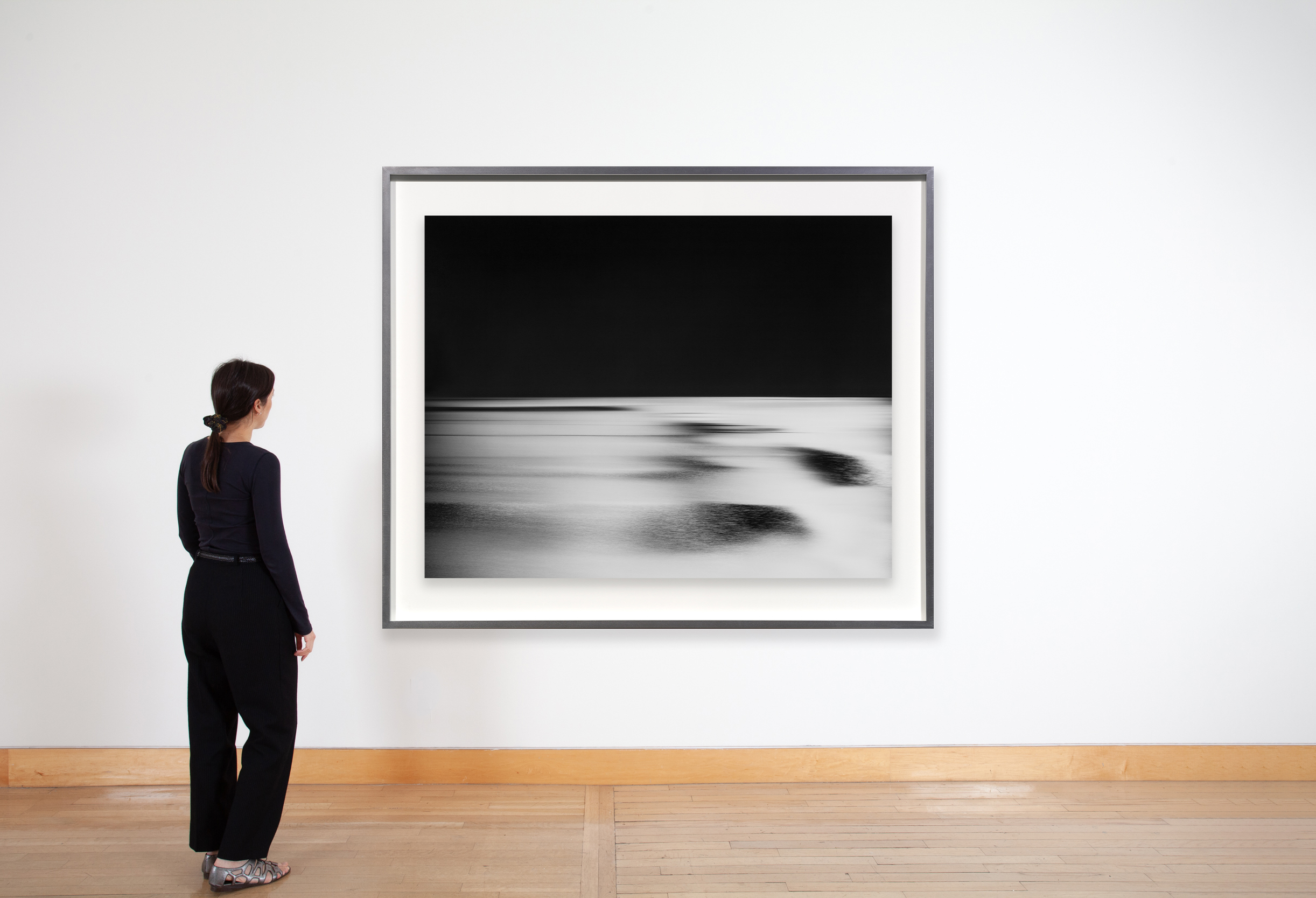 Color image of a black and white photograph of the horizon and ocean by moonlight framed in silver on white gallery wall