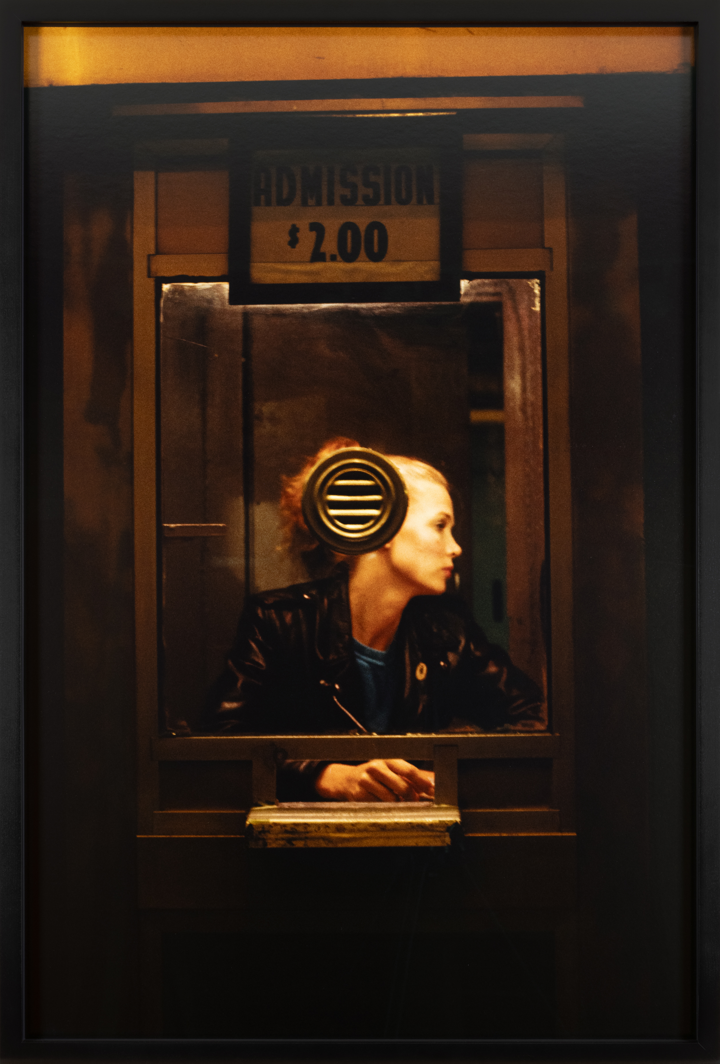 Color photograph of a silhouetted figure in a ticket booth framed in black