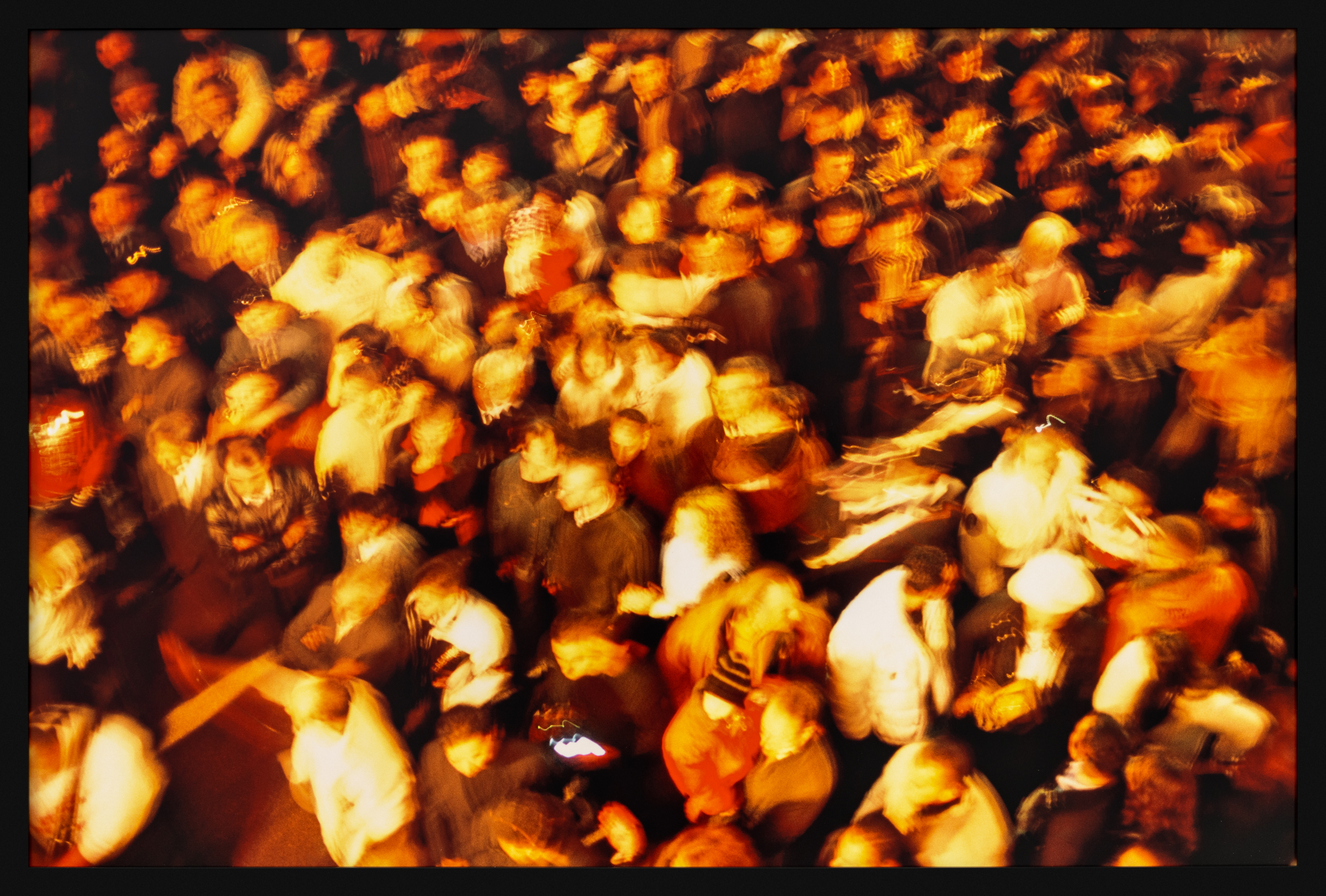 Color image depicting a warm colored crowd of people seen from above with motion blur