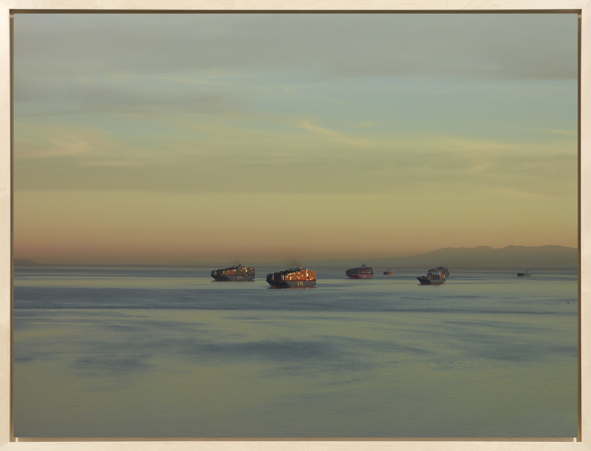 Framed color photograph of several cargo ships loaded with shipping containers on a blue expanse of water