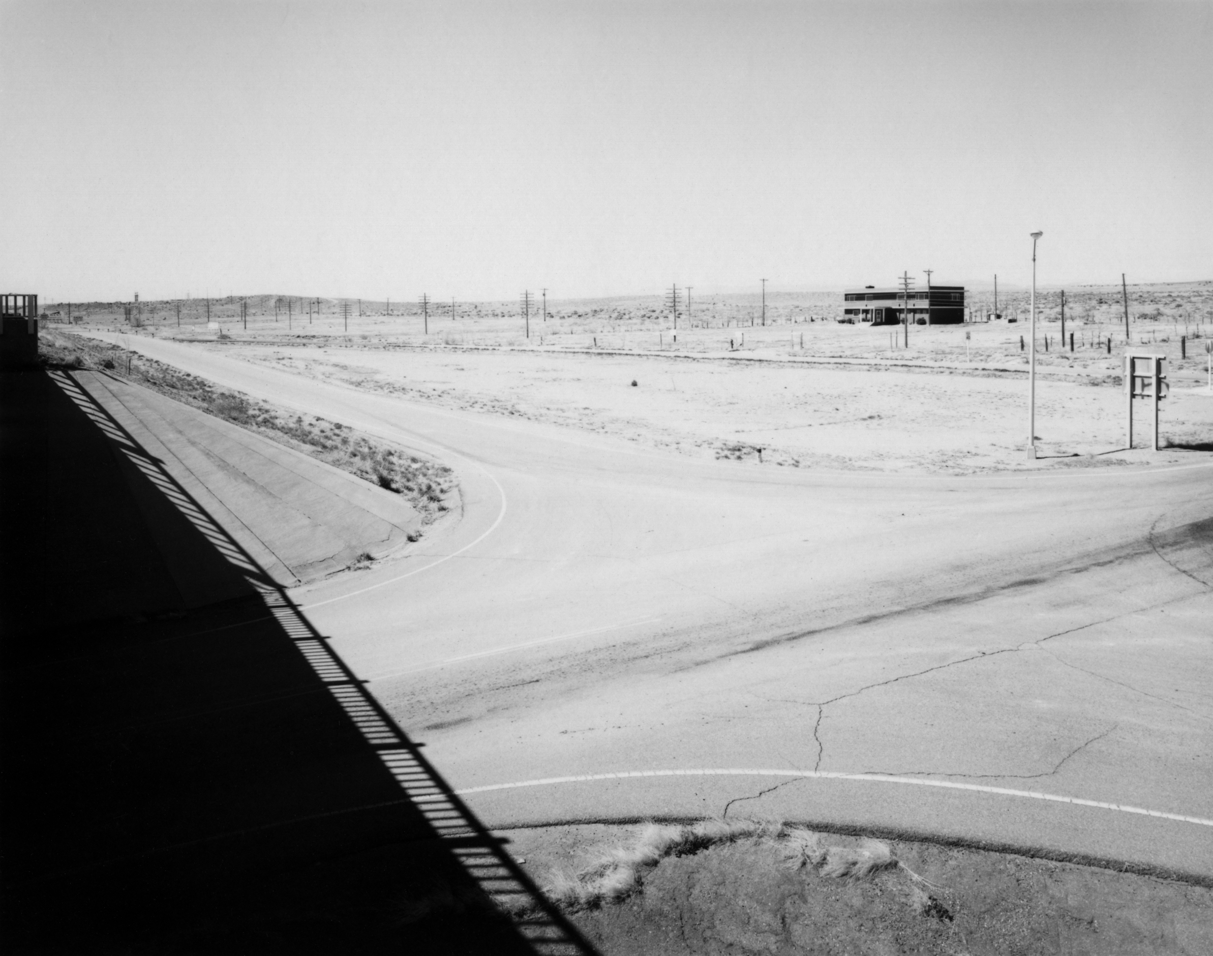 Black and white photograph of barren intersection with single building on the horizon