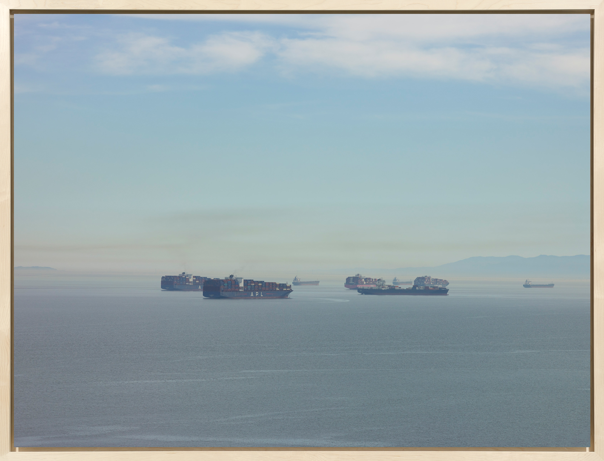 Color photograph of cargo ships on the bay during mid day framed in bleached wood