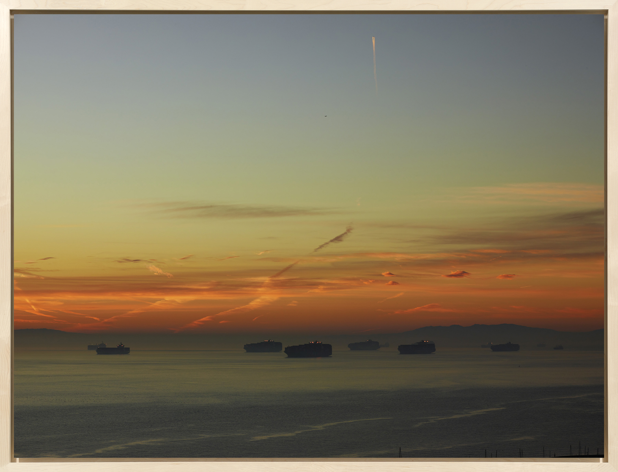Color photograph of cargo ships traveling on water early morning framed in bleached wood